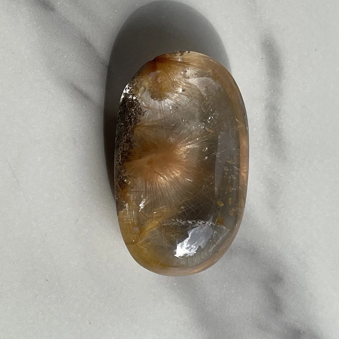 Rutilated Quartz เนื้อใสพร้อมเส้นแร่ภายใน วางถ่ายบนพื้นเรียบ
